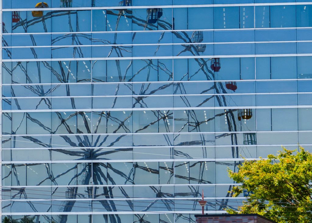 The reflection of a Ferris wheel in the mirrored windows of an office building. The differently framed windows give the reflection a mosaic look.