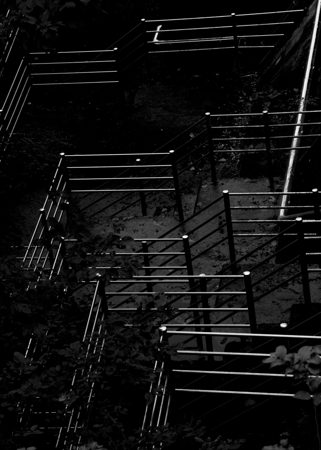 A dark, monochrome shot from above of stainless steel handrails arrange almost like a maze.